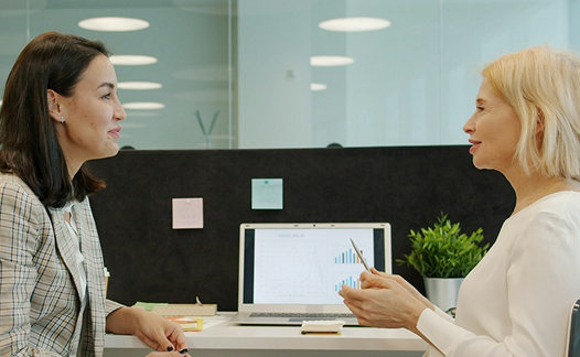 Two women facing each other on laptop